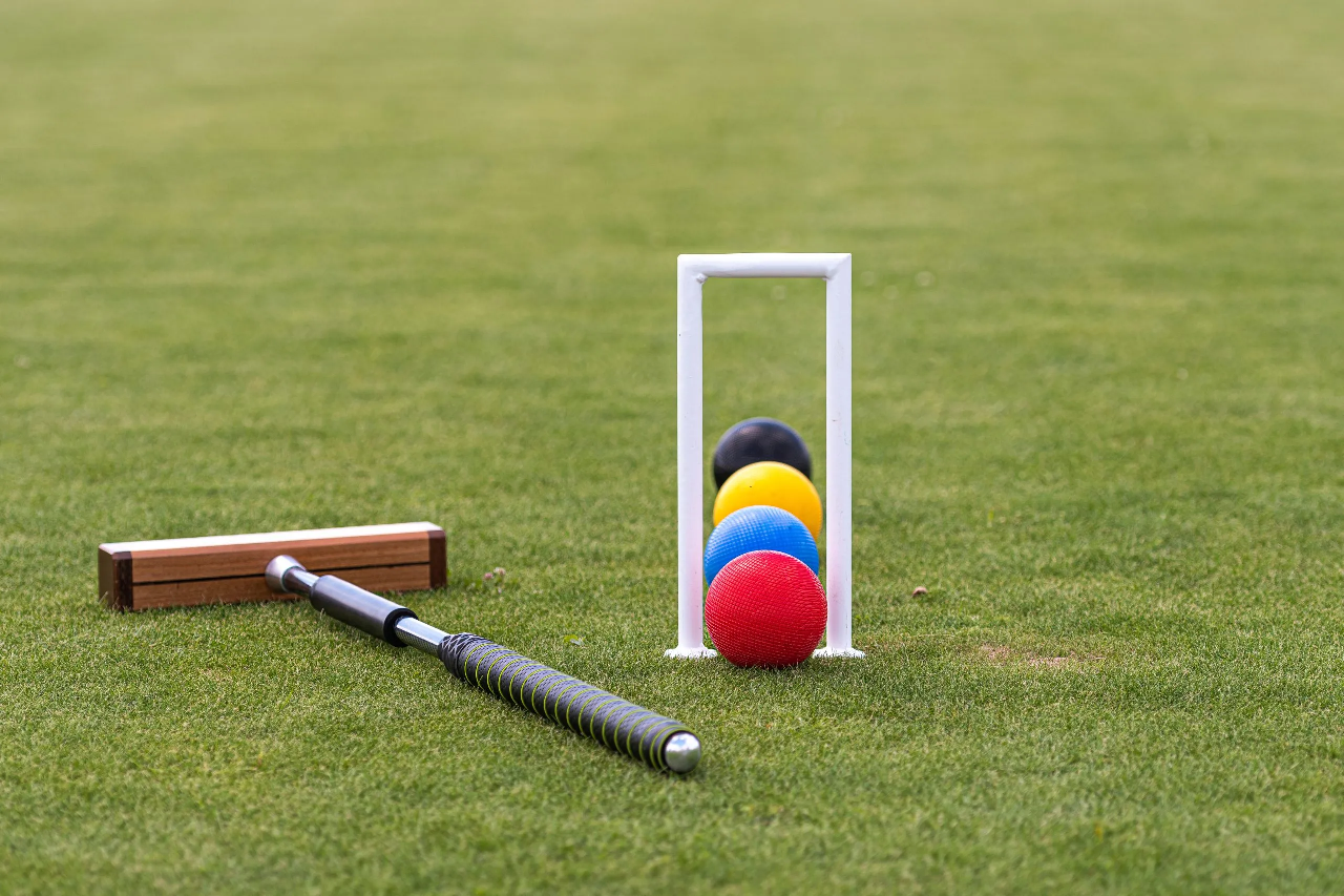 Croquet mallet and balls by a hoop on green lawn